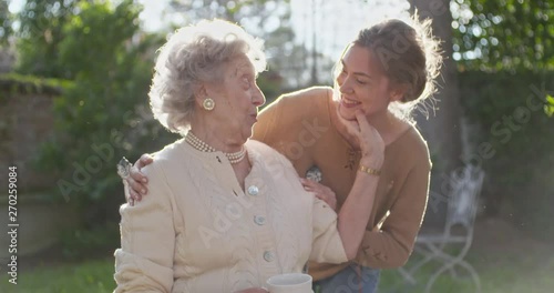 Granddaughter visiting,happy hugging grandmother at outside garden,backlight sun. Multigeneration women love holding together.White hair elderly grandma woman.Affection,togetherness,caring,loving