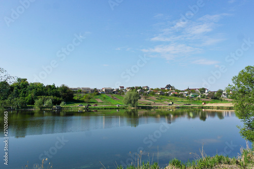 Beautiful clear lake among the village. Reflection of blue sky and plants in a lake.