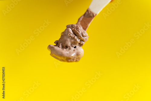 chocolate ice cream on wooden spoon on yellow background