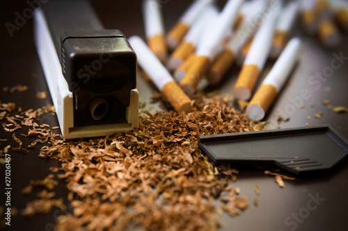 Production of cigarettes at home. The machine for cigarettes, tobacco scattered on a black background. Close-up photo