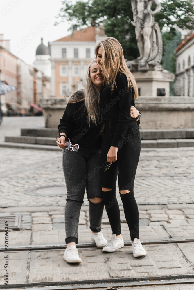 Happy friends having fun walking in city center. Beautiful young positive girls spend summer holidays. Two smiling pretty teenagers travel around old wonderful European city. Joint vacation concept