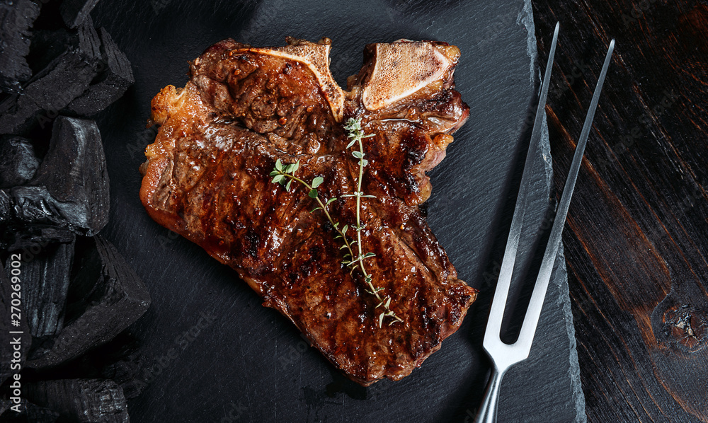 barbeque steak on a black slate board with meat fork and grill coals next to it