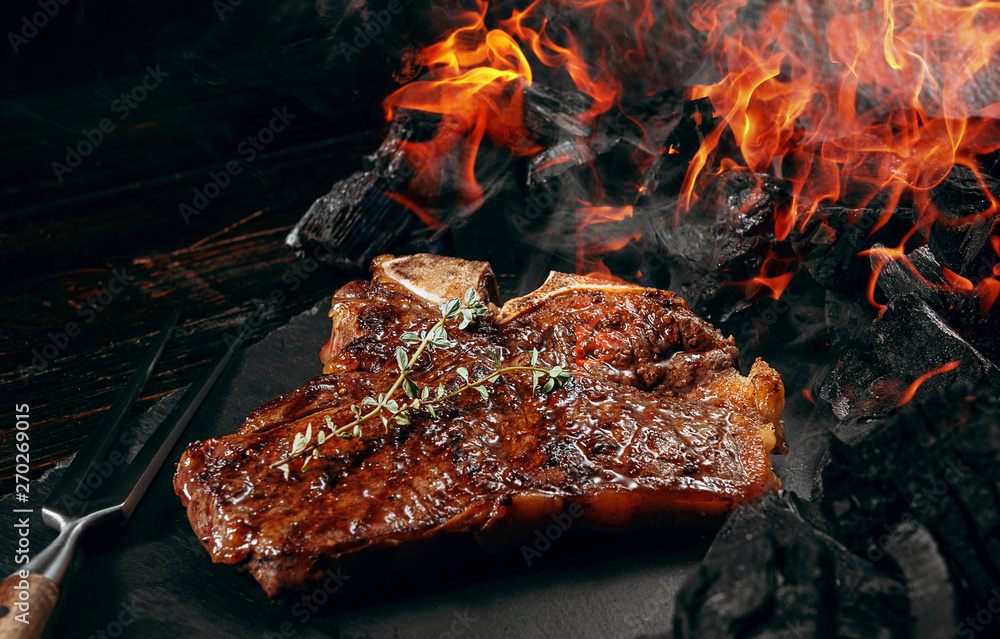 barbeque steak on a black slate board with meat fork and grill coals next to it