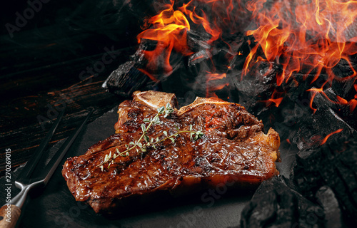 Obraz na płótnie barbeque steak on a black slate board with meat fork and grill coals next to it w salonie