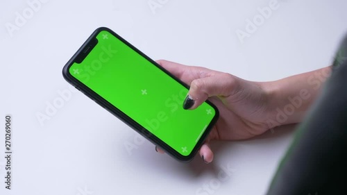 Closeup back view shoot of female hand messaging on the phone with green chroma screen in the office indoors on the white desk