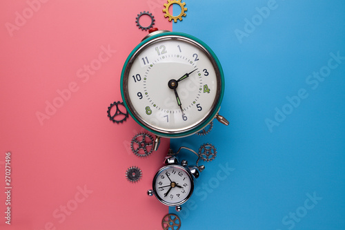 Two old alarm clocks and small gears, parts of the watch on a two-colored background photo