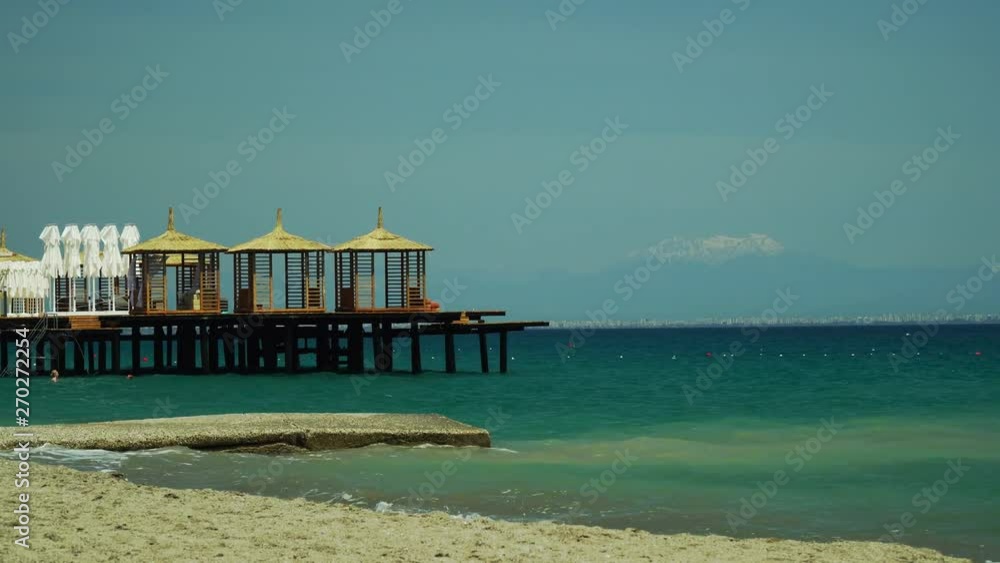Wooden pier and bungalow on the pier. In the background, far away, the city of Antalya and the mountains. Wooden pier and bungalow on the pier. In the background, far away, the city of Antalya and the mountains.