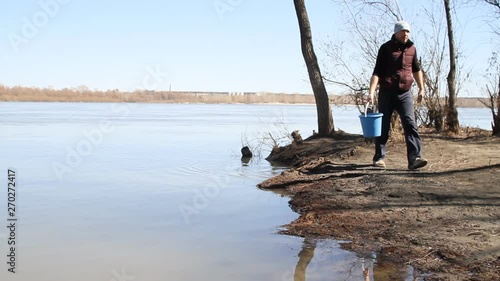 a man carries a bucket of water from the river and pours on the car photo