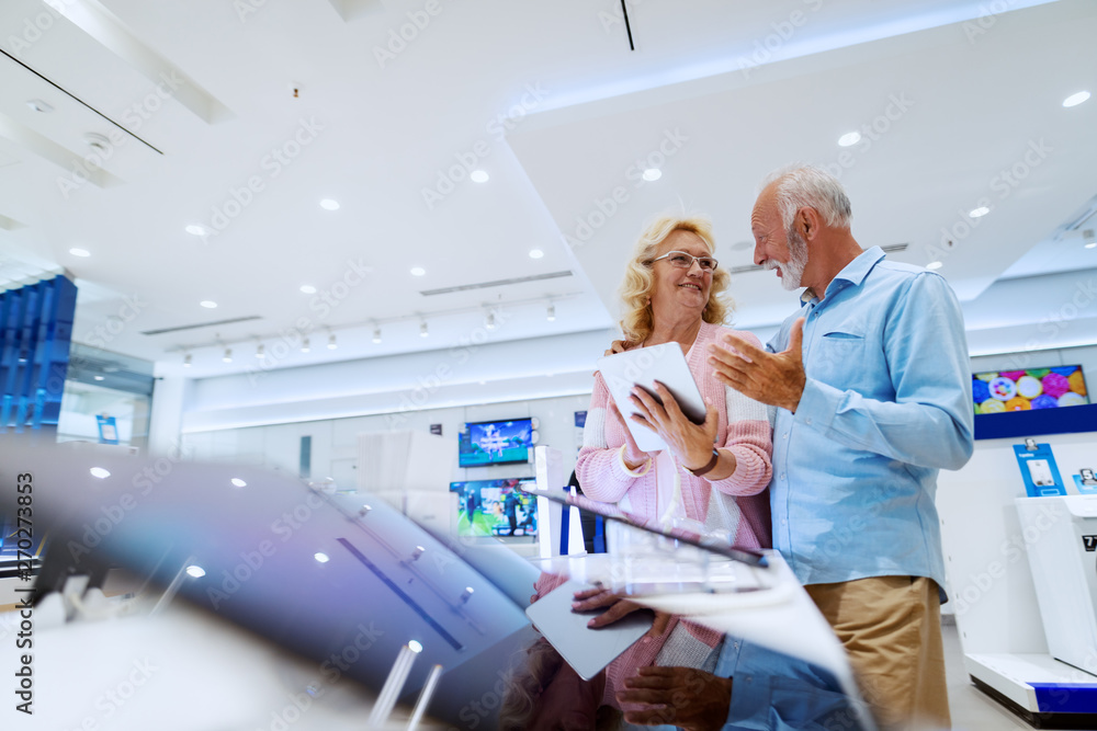 Obraz premium Happy smiling senior choosing new tablet while standing in tech store.