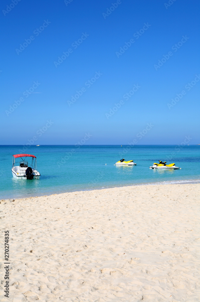A motor boat and waverunners bobbing off the beach on a beautiful tropical island. Summer Beach Water Sports