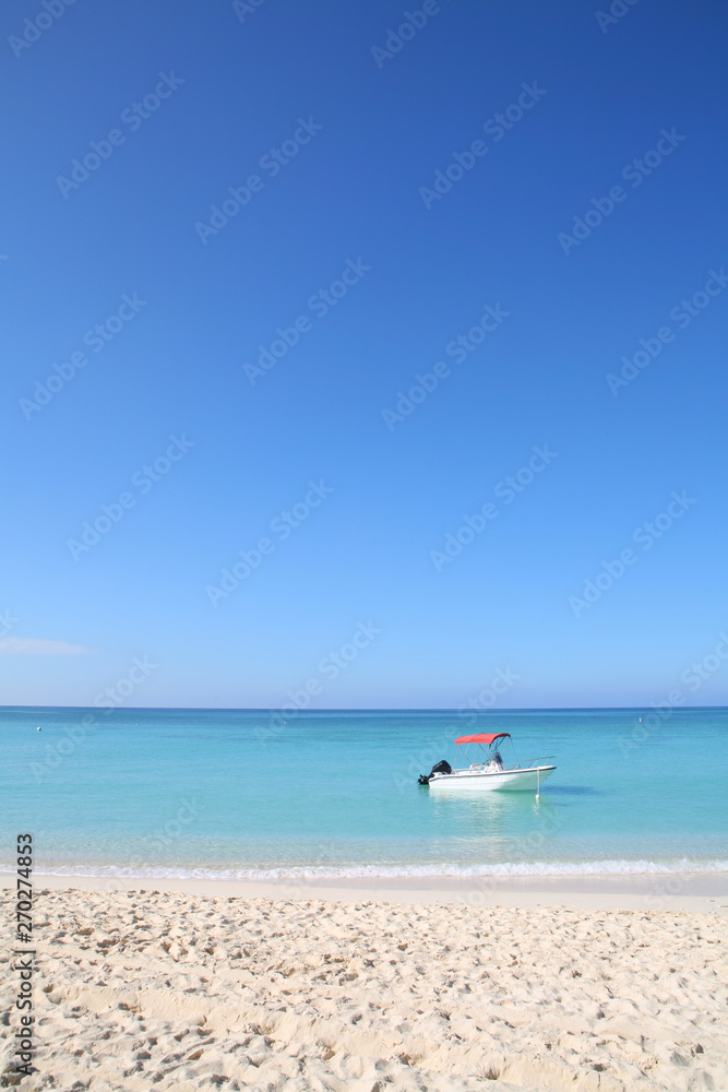 Boat Bobbing Off A Sunny Sandy tropical Beach in turquoise ocean with cloudless blue sky in the background.