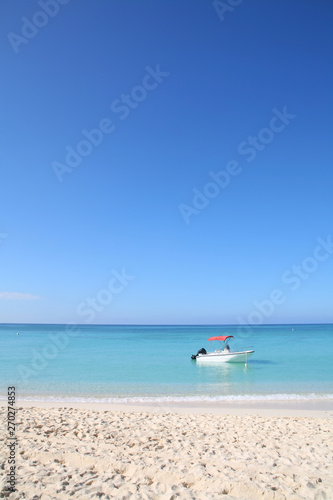 Boat Bobbing Off A Sunny Sandy tropical Beach in turquoise ocean with cloudless blue sky in the background. © allister