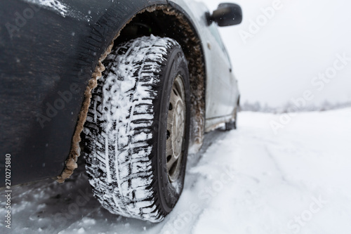 View focused on the car tire and bumper on winter road covered with snow. Vehicle on snowy road after snowfall.