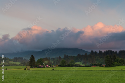 A rural scene of green farms, fields, and forests at sunset under beautiful pink and purple clouds near Tillamook, Oregon photo