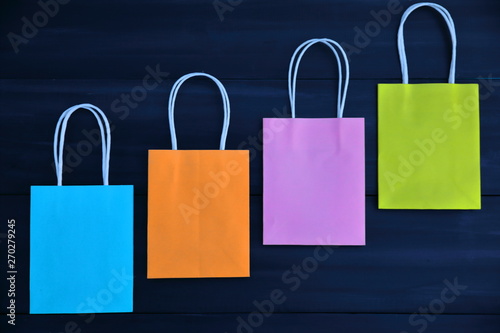 Blue, orange, pink and yellow gift bags on a dark wooden background, diagonal, top view
