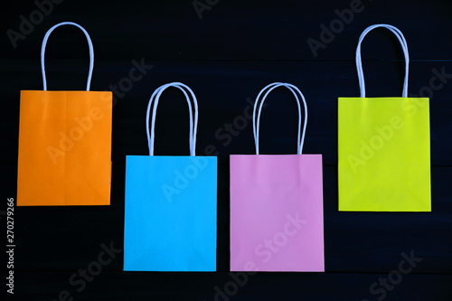 Blue, orange, pink and yellow gift bags on a dark wooden background, semicircle, top view