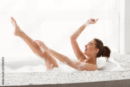 Positive Woman Shaving Legs, Resting In Bath With Foam Fototapeta