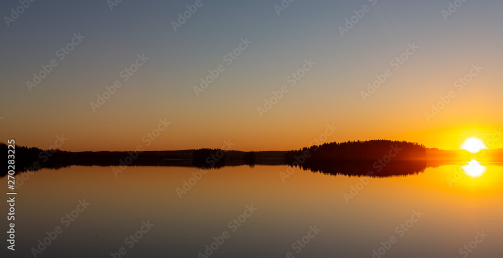 Panoramic image of sunset at the lake. Beautiful and calm reflection on the water. Silent moment during golden hour. Cover photo with copy space 