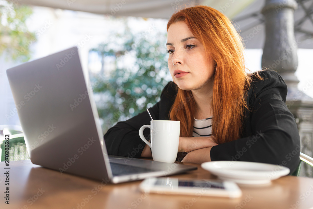 Portrait of redheaded young woman at pavement cafe looking at laptop Portrait of redheaded young woman at pavement cafe looking at laptop
