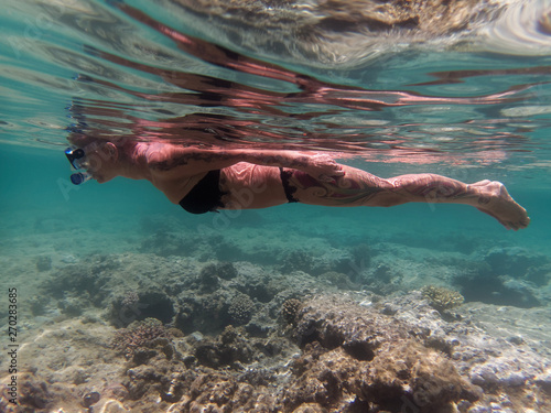 Mature slim sportive woman with tattoos and short hair snorkeling. German tourist in Egypt. Underwater photo in Hurghada, Egypt. Full body, side view