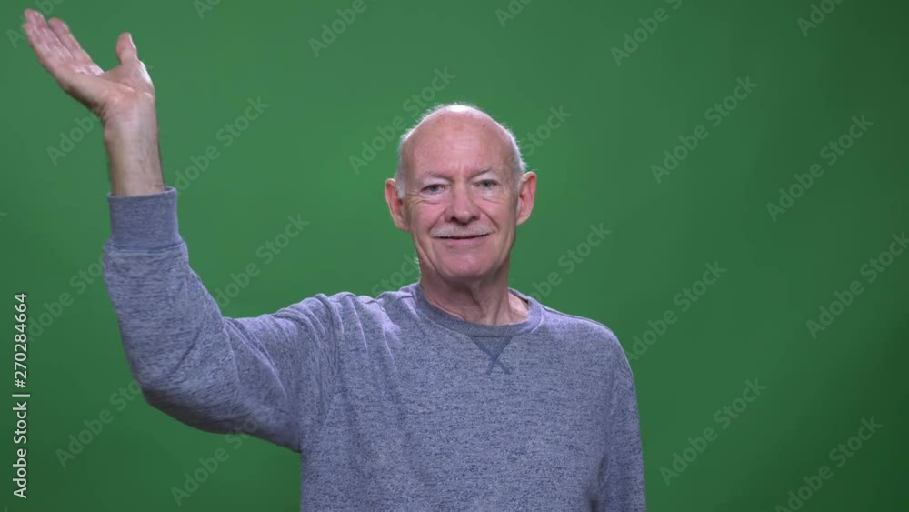 Closeup shoot of old senior caucasian man waving hi looking at camera with background isolated on green Closeup shoot of old senior caucasian man waving hi looking at camera with background isolated on green