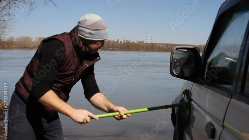 a man washing an SUV with a MOP and a rag from the bucket on the river photo