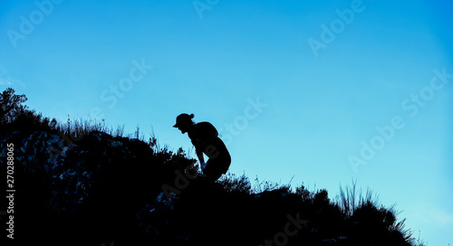 Dramatic silhouette of a person hiking and climbing a steep mountain