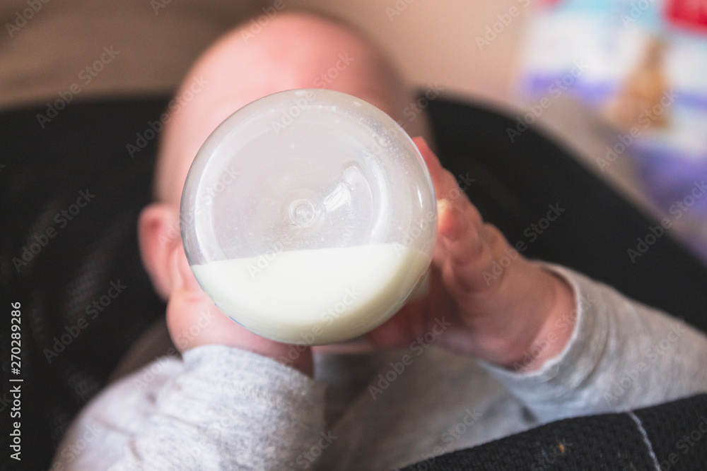 A small child drinks milk from a plastic bottle, holding with hands. Food for the child. Front view A small child drinks milk from a plastic bottle, holding with hands. Food for the child. Front view