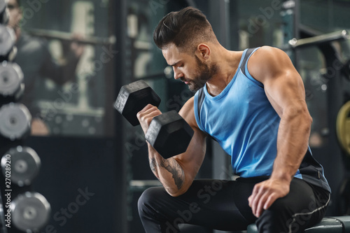 Bodybuilder pumping his biceps with dumbbell in gym