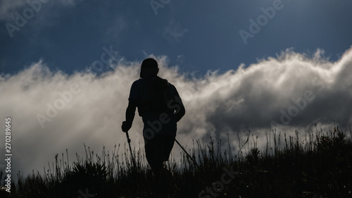 Trail runner using hiking poles on a mountain with dramatic clouds