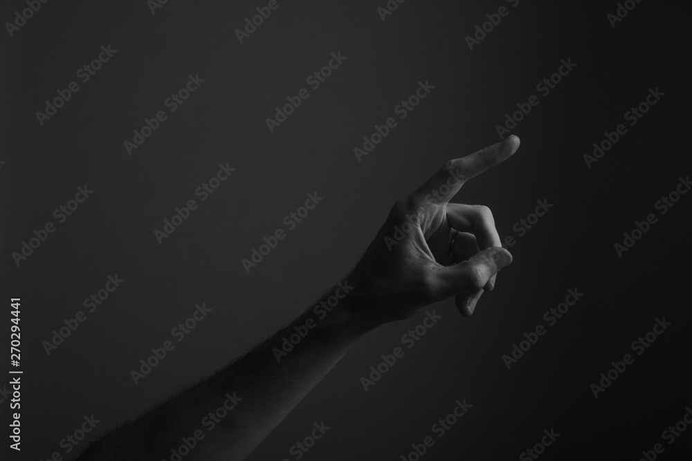 © ink drop - Male hand pointing a finger against a dark background. Selecting, touching
