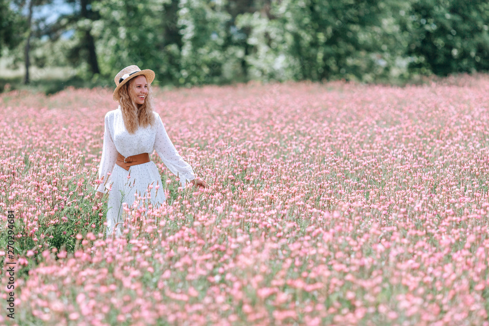 A smiling girl in a white polka dot dress and a hat in a soft pink flowering field of sainfoin. A smiling girl in a white polka dot dress and a hat in a soft pink flowering field of sainfoin.
