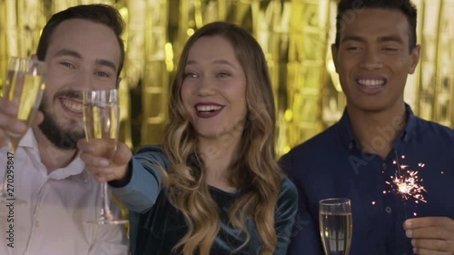 4 happy cheerful people at a party with a bottle of wine light a sparkler. a group of laughing people of mixed race on a gold background. HD photo