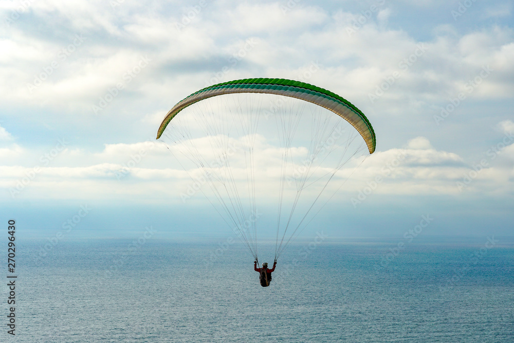 Man doing sport (Para-glider). Man paragliding in the clouded sky. Paragliding is an extreme sport and recreation. Torrey Pines Gliderport. San Diego. California, USA. Man doing sport (Para-glider). Man paragliding in the clouded sky. Paragliding is an extreme sport and recreation. Torrey Pines Gliderport. San Diego. California, USA.