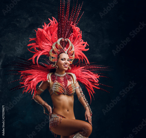Young attractive brasil dancer in red feather costume is dancing at small dark studio.