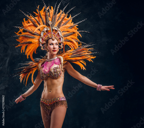 Beautiful young female in special feather costume is dacing at studio.