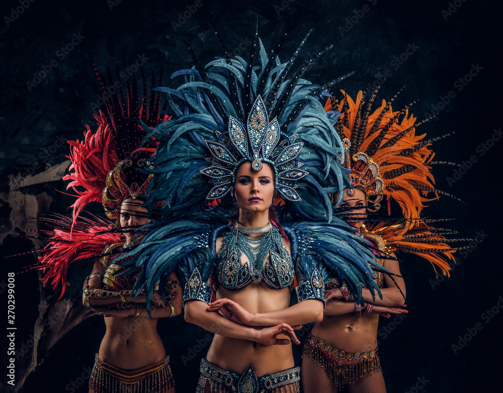 Three beautiful young womans in traditional brasilian carnaval costumes are posing for photographer at studio.