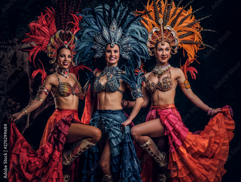 Three beautiful young womans in traditional brasilian carnaval costumes are posing for photographer at studio.
