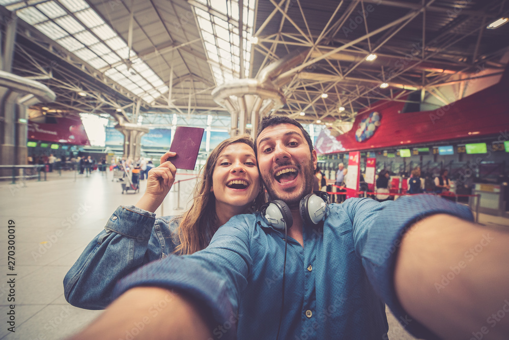 Beautiful young tourist couple in international airport, taking selfie with passport and boarding pass ready for boarding in the airplane and fly. Travel around the world concept.