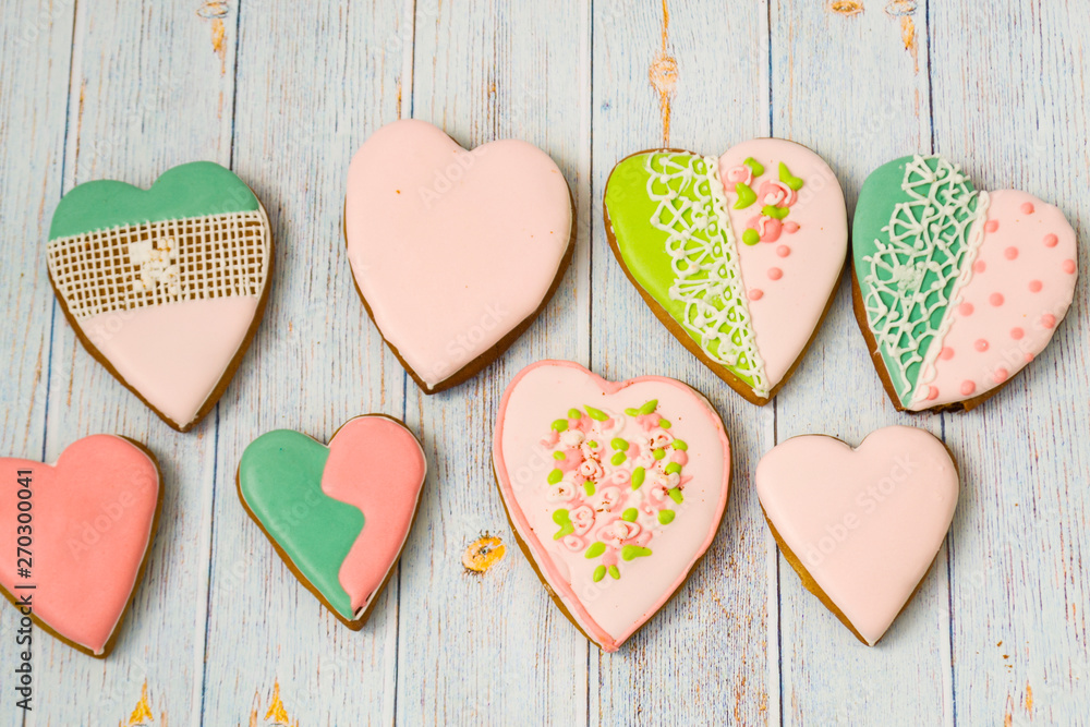 Fototapeta premium Pink and colored gingerbread and honey cakes and biscuits. Heart-shaped lie on a light wooden background. Patern. Place for text. The concept of love, mother's day, cooking,