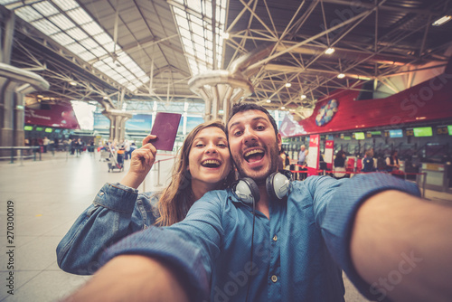 Beautiful young tourist couple in international airport, taking selfie with passport and boarding pass ready for boarding in the airplane and fly. Travel around the world concept.