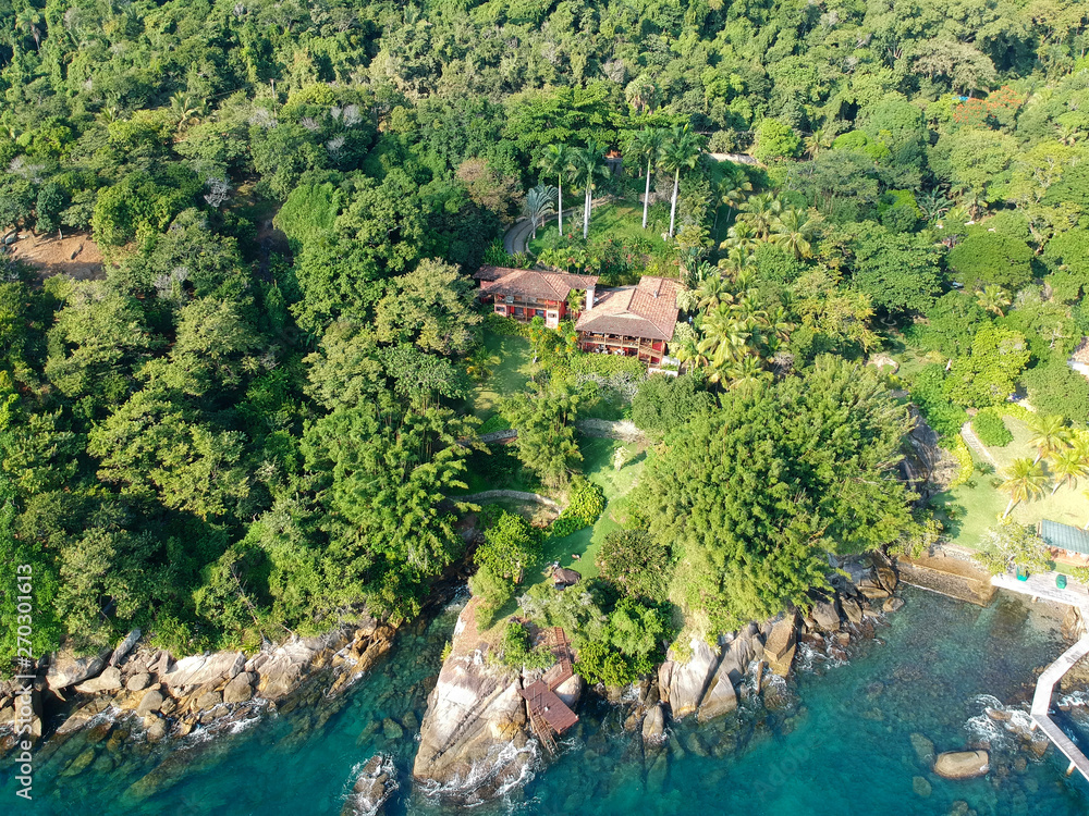 Aerial view of tropicsal house in forest surrounded by trees and next to the ocean and blue turquoise water. luxurious villa and spacious pavilion next to the sea, Brazil.