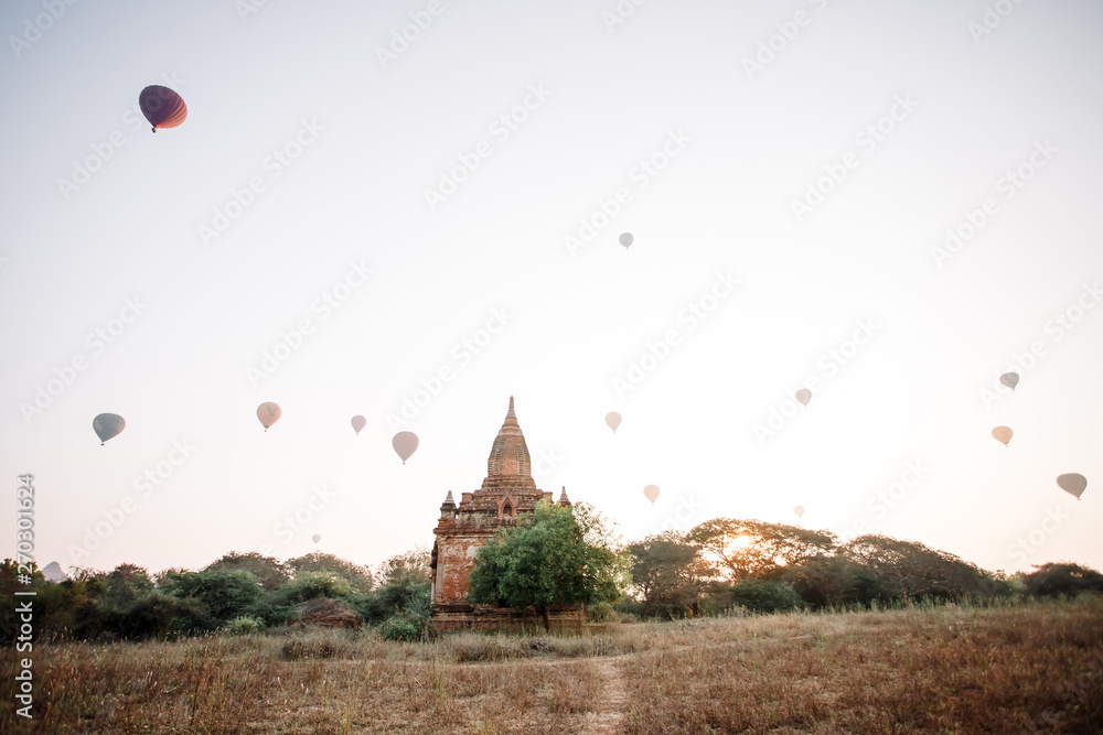 Hot air balloon over the foggy morning around Temple in Bagan, Myanmar. Balloons fly over thousands of ancient pagodas. Dawn in Bagan, misty. Tourists are watching the sunrise over the ancient city.