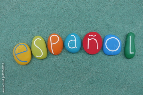 Español, spanish language word composed with multi colored stones over green sand