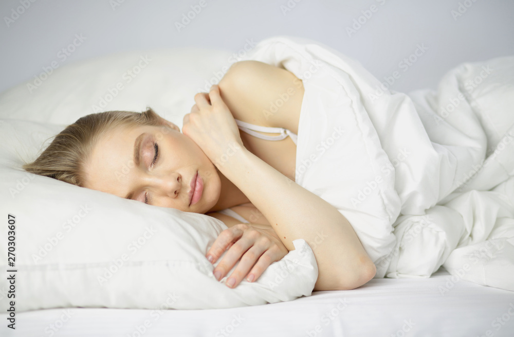 Sleep. Beautiful young woman sleeping in bed in the morning. Portrait of an attractive girl resting in a comfortable bed with a pillow and white bedding. Bedroom. Copy space for your text Sleep. Beautiful young woman sleeping in bed in the morning. Portrait of an attractive girl resting in a comfortable bed with a pillow and white bedding. Bedroom. Copy space for your text