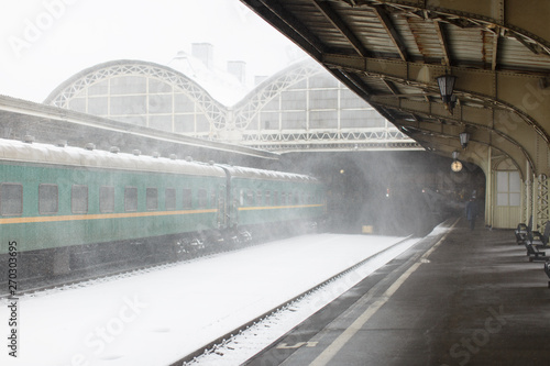 Empty railway platform at Train Station with passenger train in blizzard, bad weather.