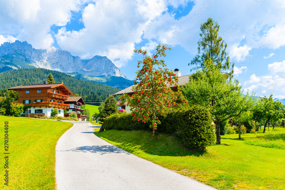 Road and traditional alpine houses in village of Going am Wilden Kaiser on beautiful sunny summer day with Alps mountains in background, Tirol, Austria