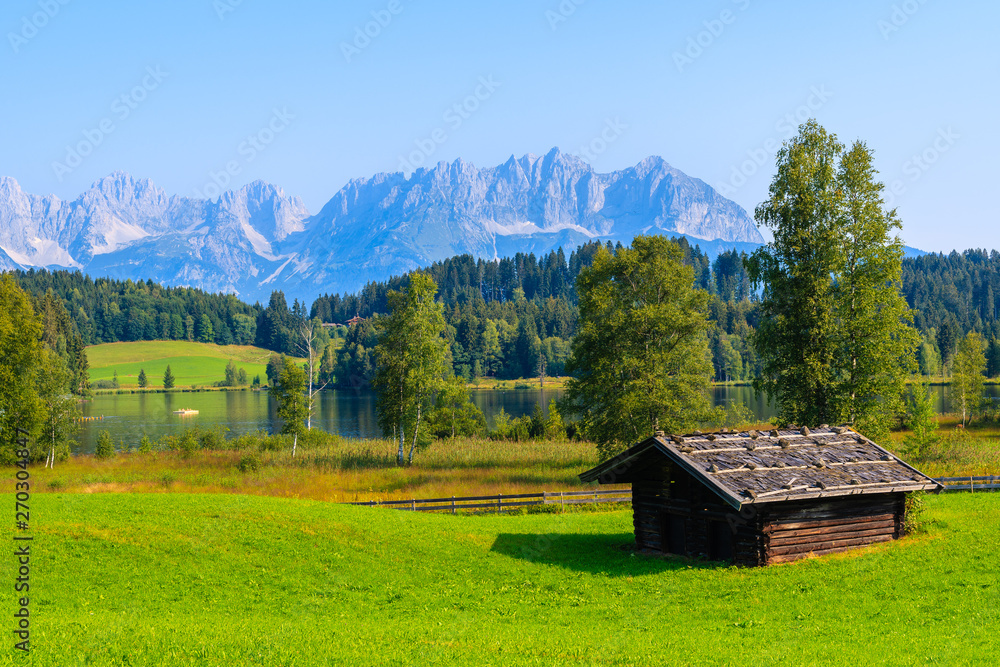 Typical alpine old wooden hut on green meadow near Schwarzsee lake lake on sunny summer day, Tirol, Austria