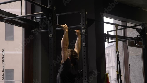 Closeup side view shoot of adult muscular athletic bodybuilder training and lifting himself on the bars indoors in the gym