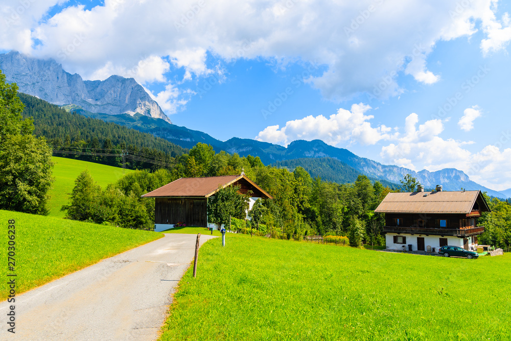 Road and traditional alpine houses in village of Going am Wilden Kaiser on beautiful sunny summer day with Alps mountains in background, Tirol, Austria